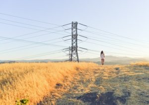 woman walking in field underneath power lines