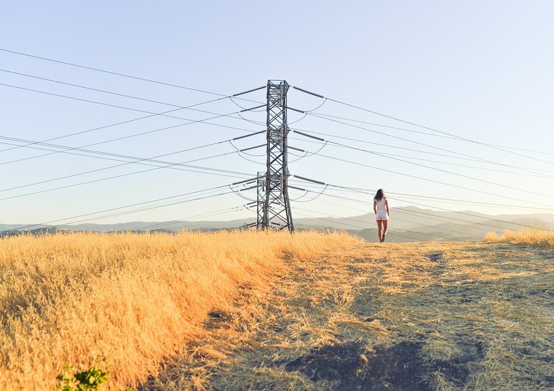 woman walking in field underneath power lines